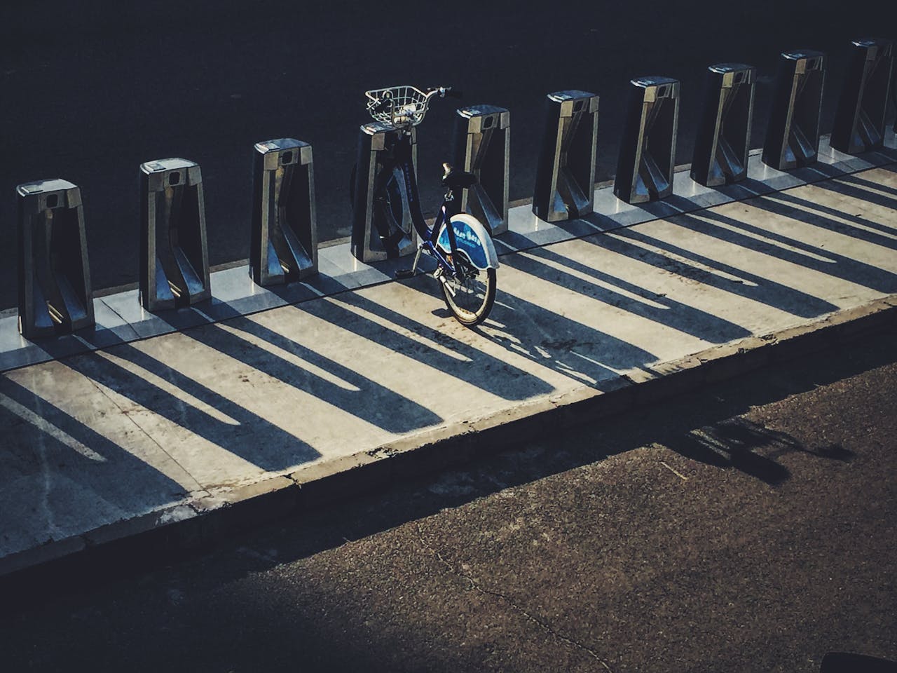 A lone bicycle in a row of stands casts long shadows on a sunny street in Daxing District, Beijing.