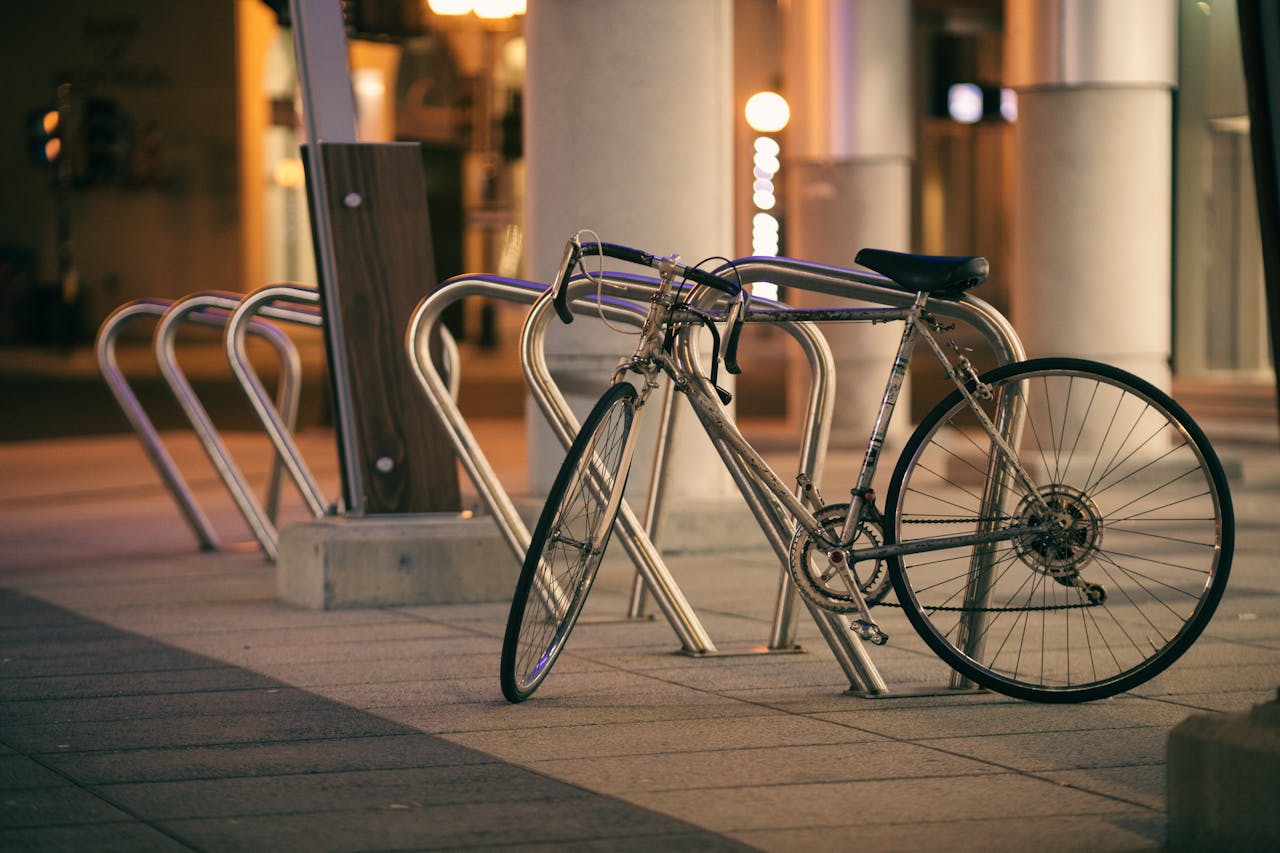 A bicycle parked at a rack on a city sidewalk at night, under warm lights.